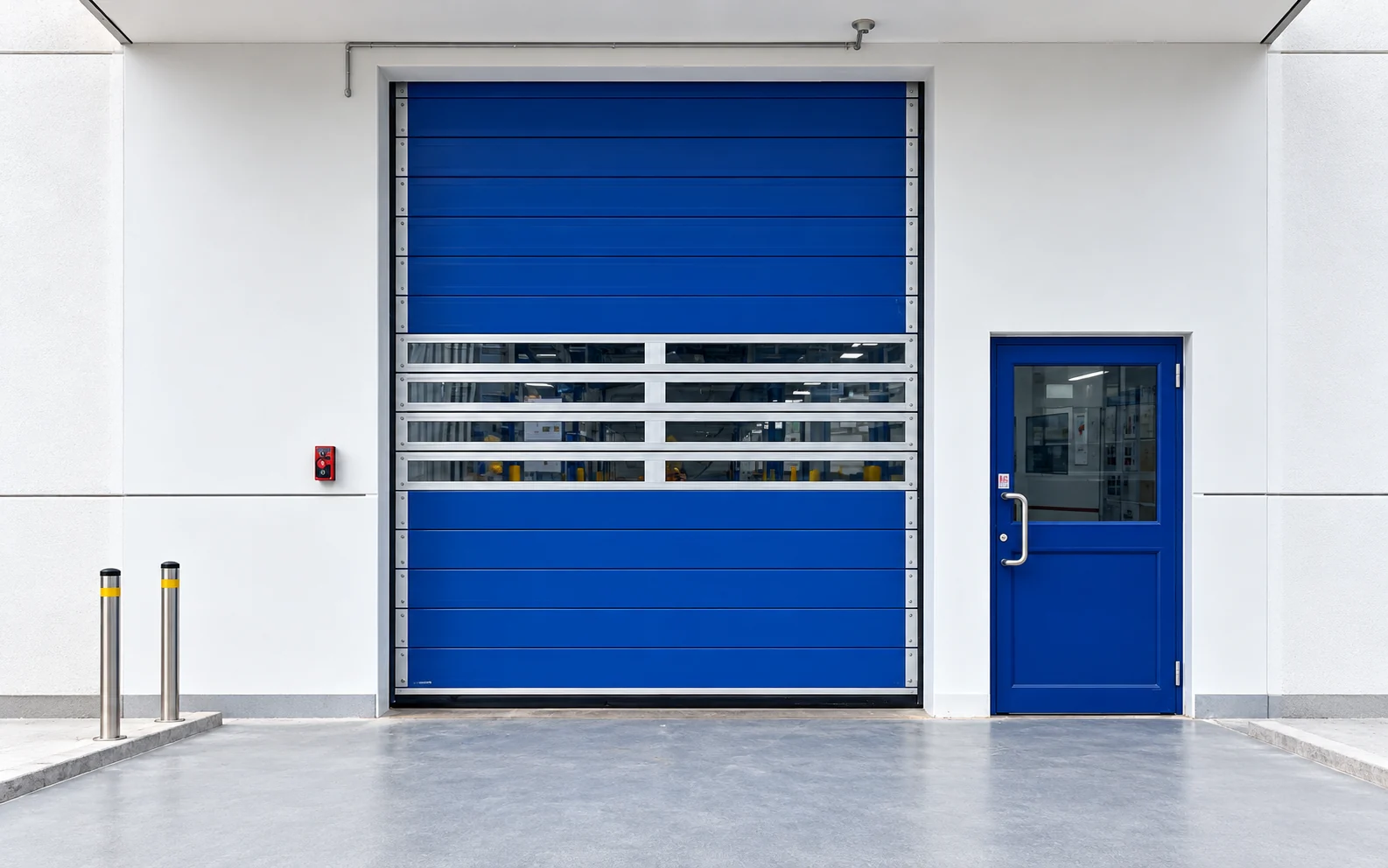 Blue spiral high speed roll-up door with a white frame and enclosed headbox beside a pedestrian door at a factory entrance