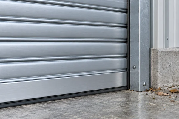 Close-up illustration of aluminum shutter slats, bottom seal, and side guide with debris at floor level